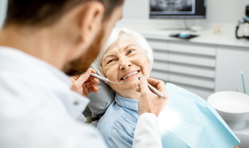 Senior patient smiling during a dental check-up with a dentist using professional tools in a modern clinic.