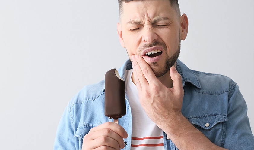 Man clutching jaw in pain while holding a chocolate ice cream bar, illustrating tooth sensitivity