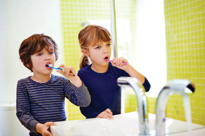 Two young children brushing their teeth at a bathroom vanity to maintain oral hygiene and prevent tooth decay