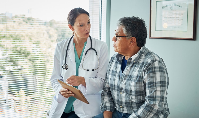 Female doctor discussing medical results on a digital tablet with a senior patient during a clinical consultation in a healthcare facility.