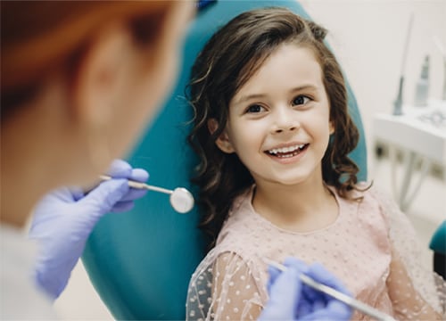 Smiling girl sitting in a dental chair while a paediatric dentist shows her dental instruments during a child-friendly dental visit.