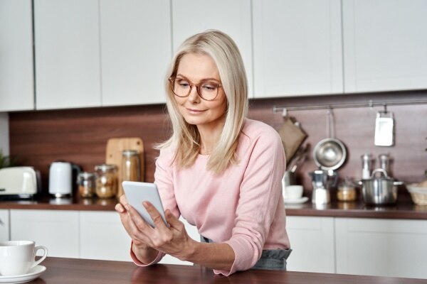Woman with glasses using a smartphone in a modern kitchen.