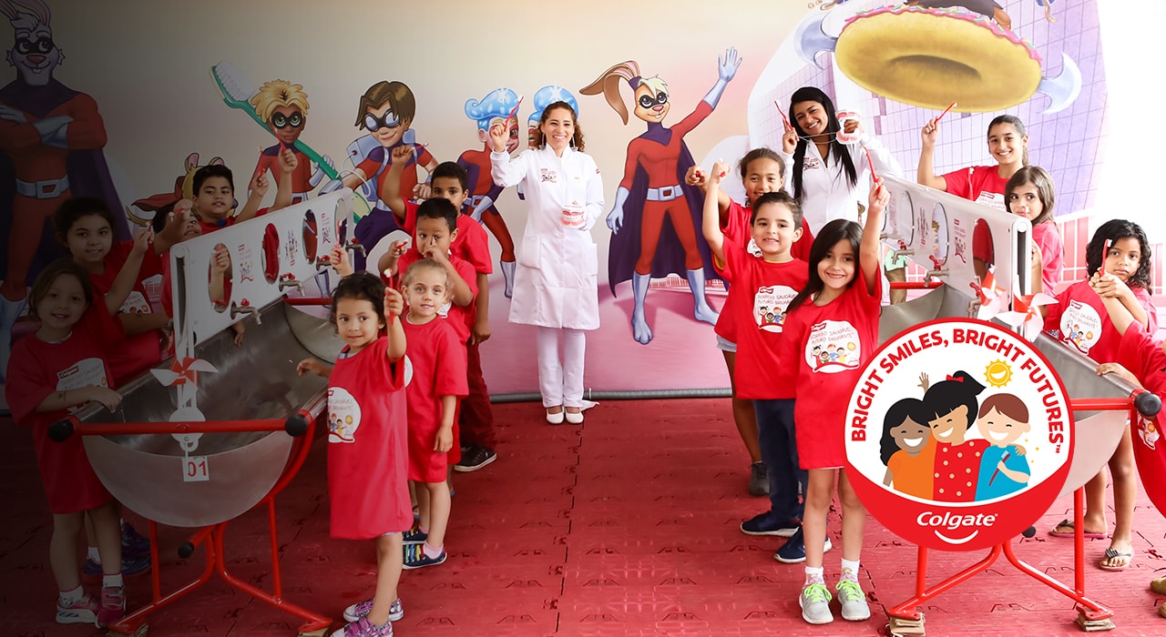 children smiling and holding a Colgate toothpaste box in a classroom