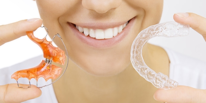 Beautiful smiling girl holding retainer for teeth 