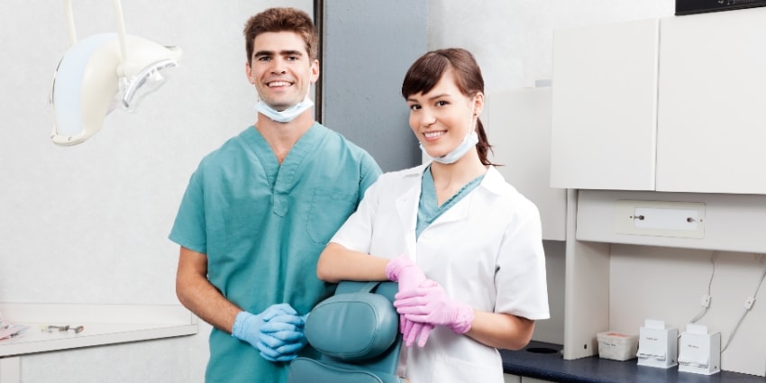 Two young dentists smiling by dental chair at clinic