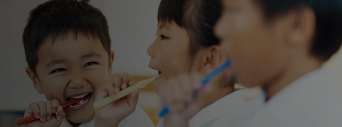 Two children, boy, and girl smiling at each other brushing their teeth