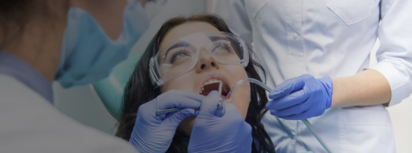 A dental professional wearing safety PPE gear and white lab coat smiling compassionately A dental professional wearing safety PPE gear and white lab coat smiling compassionately